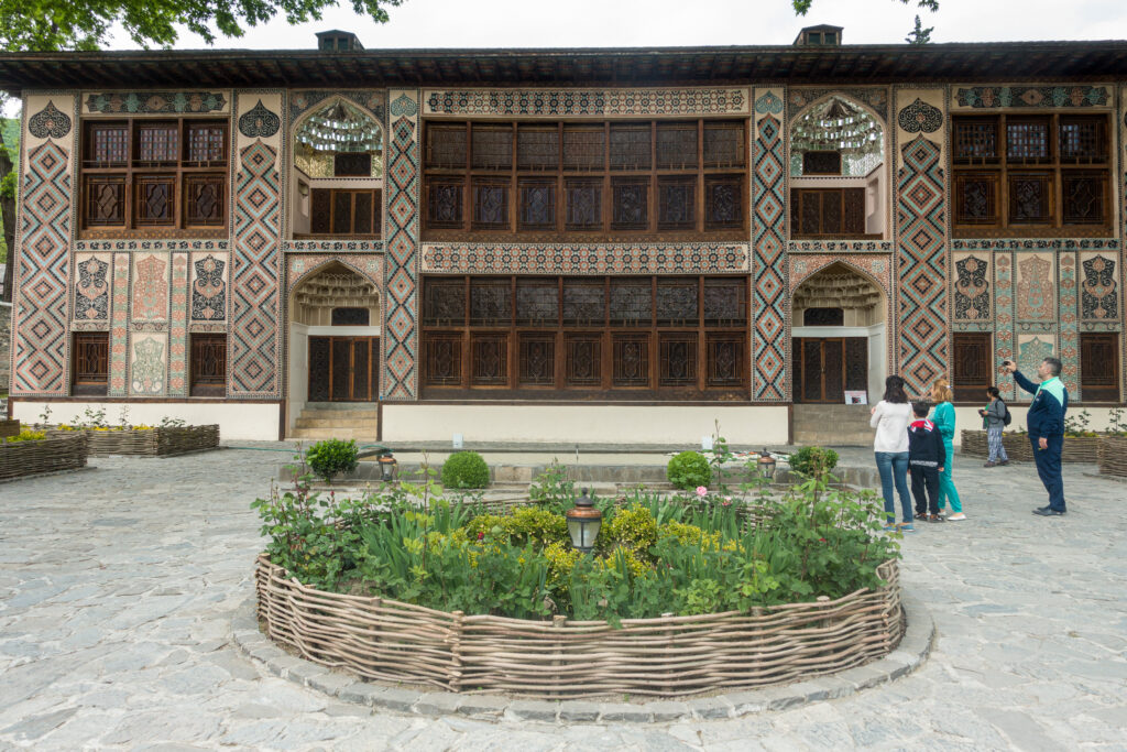 View of the outside of Palace of the Sheki Khans with ornate tiles and a flower bed in front - Sheki Azerbaijan